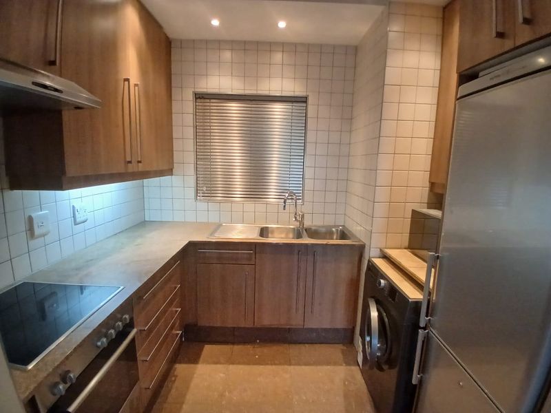 Compact kitchen featuring wood-finish cabinetry, tiled backsplash, integrated oven and hob, and a stainless steel sink with a window view.