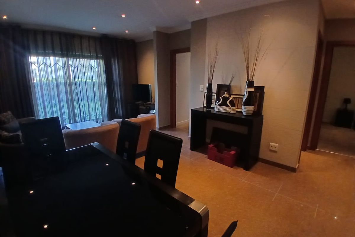A well-lit living area featuring tiled flooring, recessed downlights, and a sliding glass door with security gate leading to the exterior.