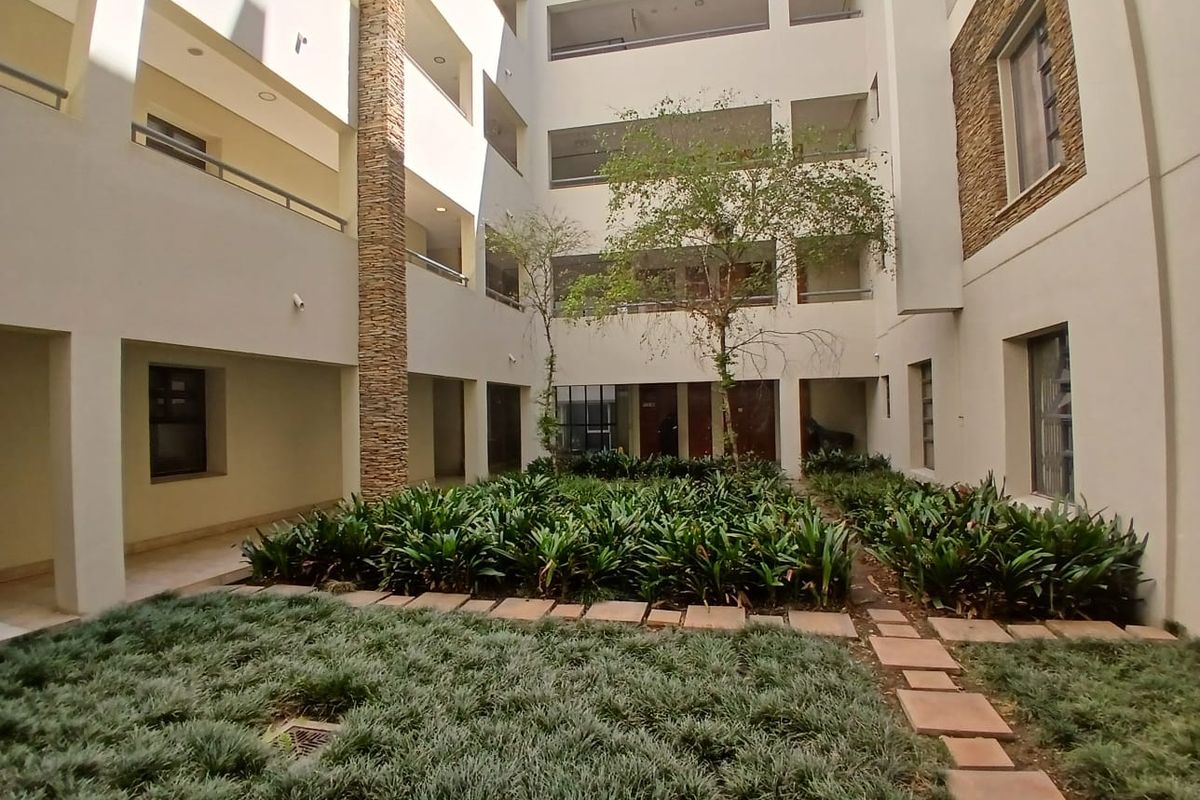 A well-maintained central courtyard within an apartment complex, featuring stone-clad pillars, landscaped garden beds, and private balconies overlooking the space.