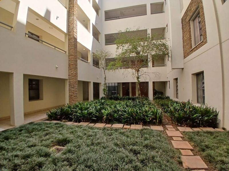 A well-maintained central courtyard within an apartment complex, featuring stone-clad pillars, landscaped garden beds, and private balconies overlooking the space.