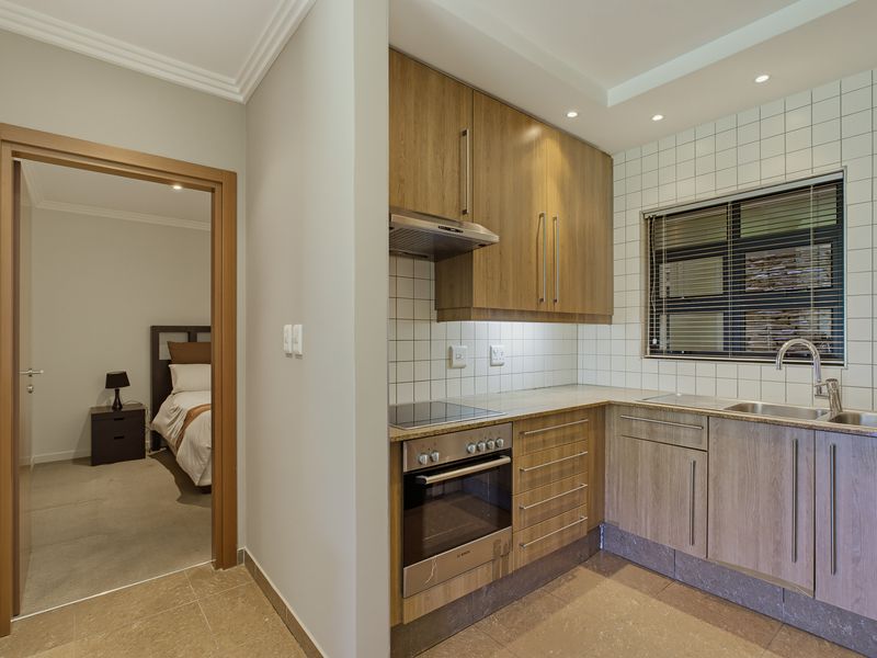 A well-maintained kitchen featuring modern wood-finish cabinetry, integrated appliances, and a tiled backsplash, with an adjacent view into a bedroom.