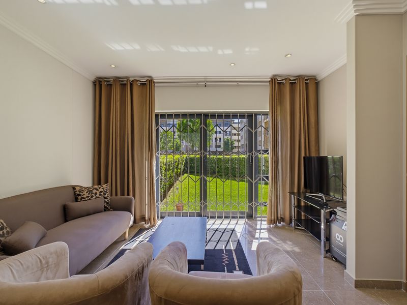 A bright living room featuring tiled flooring, recessed lighting, and a sliding glass door with a security gate leading to a private garden area.