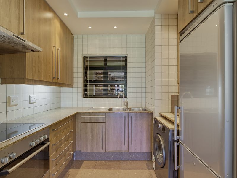 A modern, well-maintained kitchen featuring wood-finish cabinetry, stone countertops, integrated appliances, and a tiled backsplash with recessed lighting.