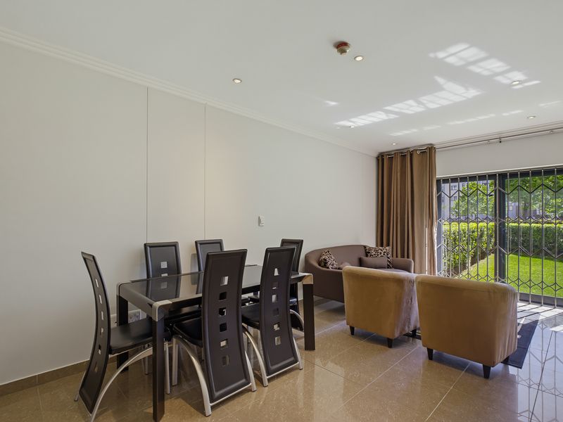 Open plan living and dining area featuring polished tiled flooring, recessed lighting, and a sliding glass door with security gate leading to the garden.