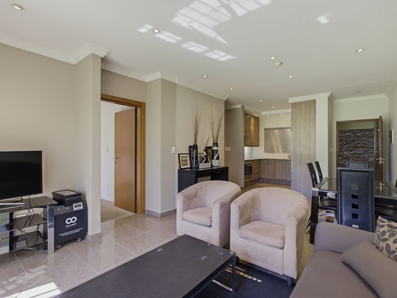 An open-plan living and dining area featuring tiled floors, recessed lighting, and a functional kitchen with built-in cabinetry and appliances.