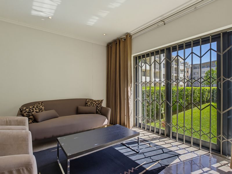 A bright living room featuring tiled flooring, recessed lighting, and a large sliding glass door with a security gate leading to the garden.