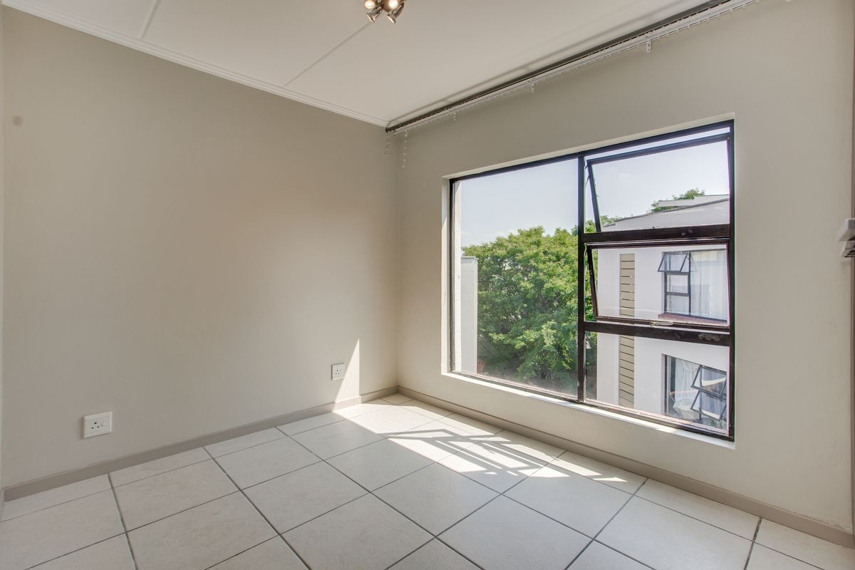 A bright, empty bedroom featuring neutral wall paint, tiled flooring, and a large window providing natural light and an exterior view.