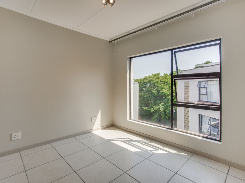 A bright, empty bedroom featuring neutral wall paint, tiled flooring, and a large window providing natural light and an exterior view.