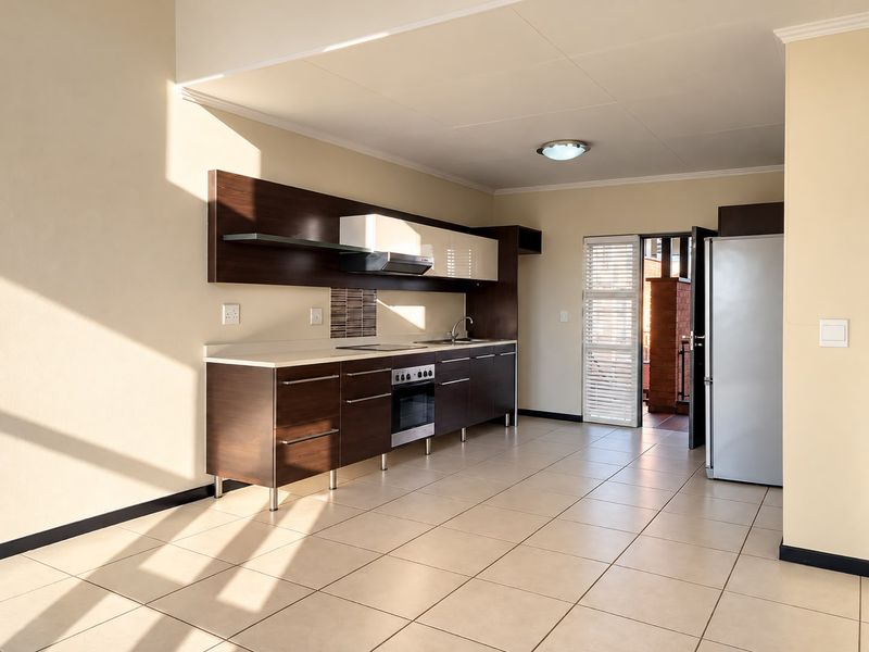 Modern kitchen featuring dark wood cabinetry, integrated oven, extractor fan, and tiled flooring, with direct access to an outdoor balcony area.