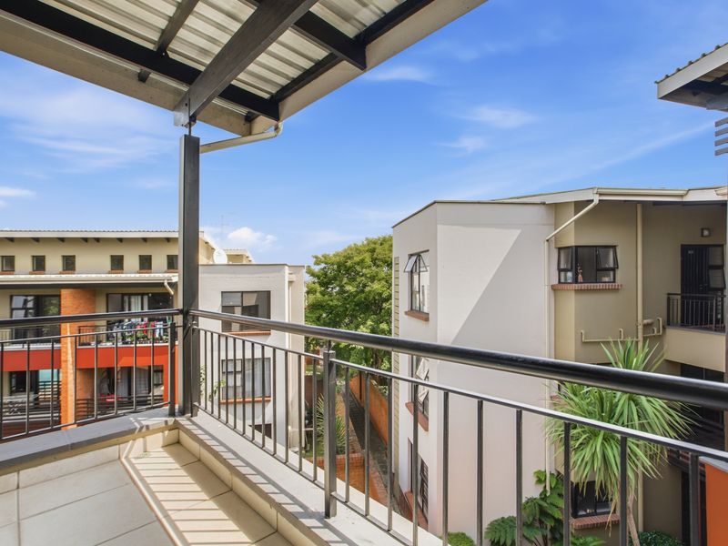 A covered balcony featuring tiled flooring and a metal balustrade, offering an elevated view of the surrounding apartment complex.