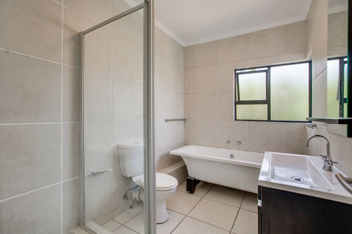 A clean and functional bathroom featuring a freestanding bathtub, a separate glass-enclosed shower, a toilet, and a vanity basin with neutral wall and floor tiling.