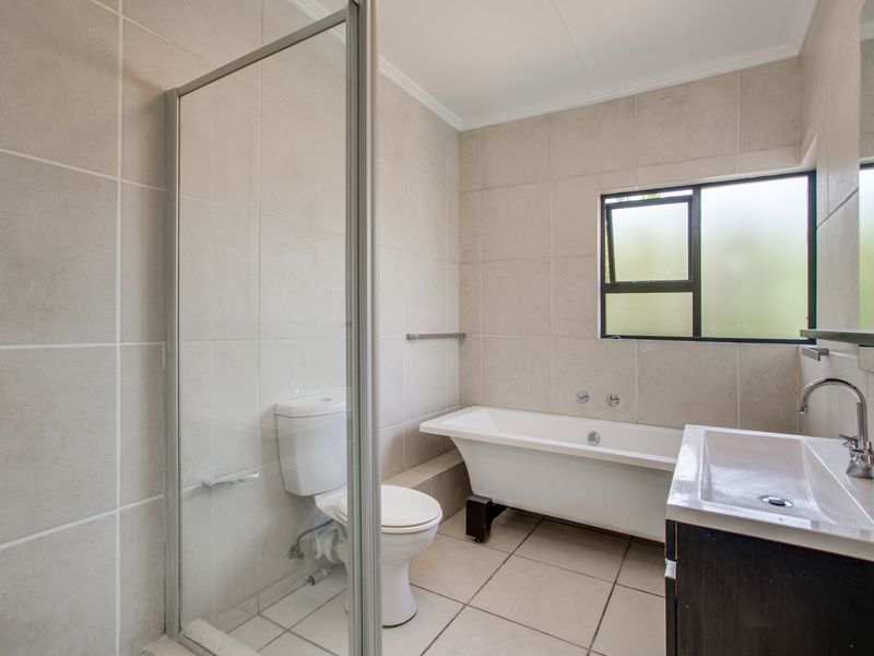 A clean and functional bathroom featuring a freestanding bathtub, a separate glass-enclosed shower, a toilet, and a vanity basin with neutral wall and floor tiling.