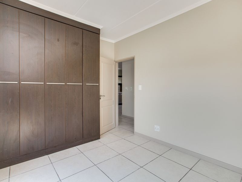 A clean, empty bedroom featuring dark wood built-in cupboards, neutral walls, and light-colored floor tiles.