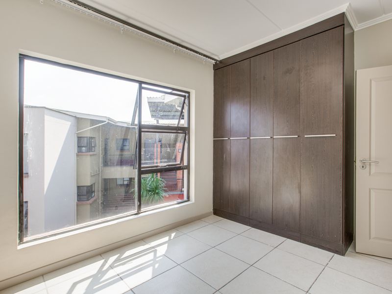 A bright, empty bedroom featuring neutral tiled flooring and dark wood built-in cupboards, offering a clean and functional space.