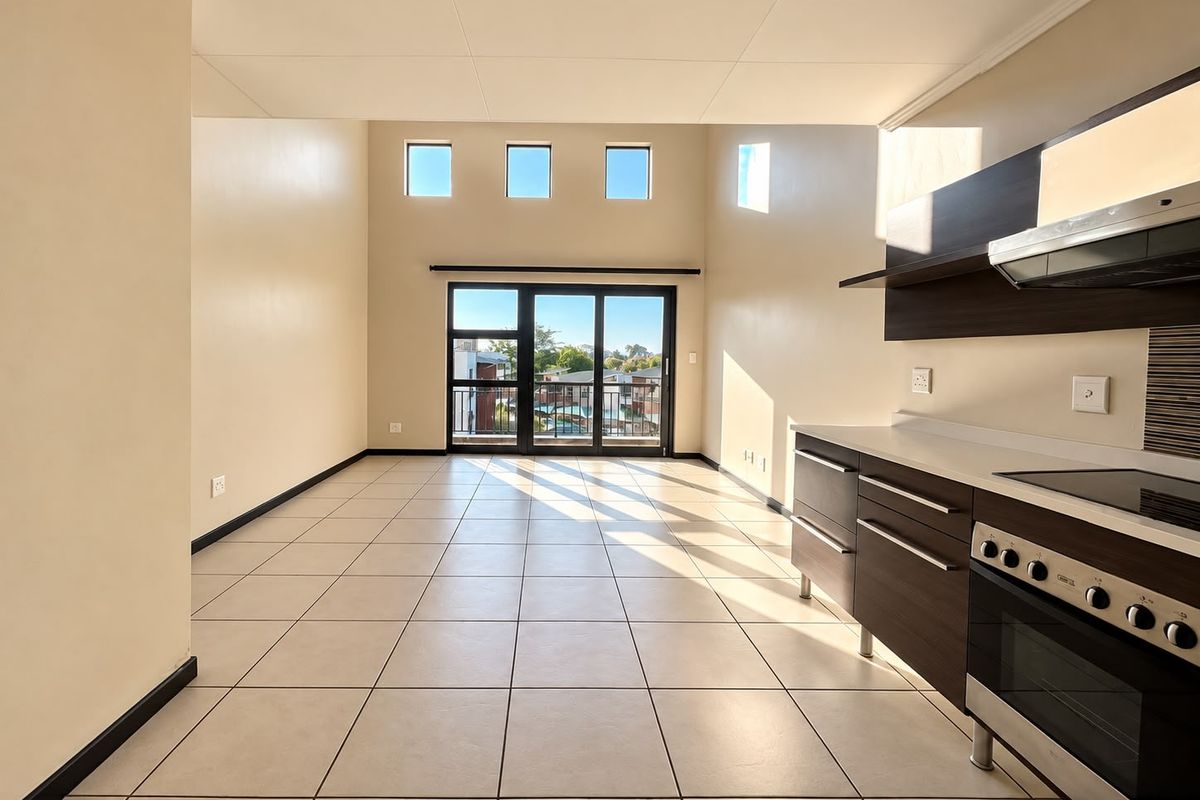 Spacious open-plan living area featuring tiled floors, modern kitchen cabinetry with built-in appliances, and large sliding doors leading to a balcony.