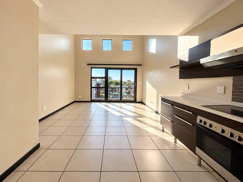 Spacious open-plan living area featuring tiled floors, modern kitchen cabinetry with built-in appliances, and large sliding doors leading to a balcony.
