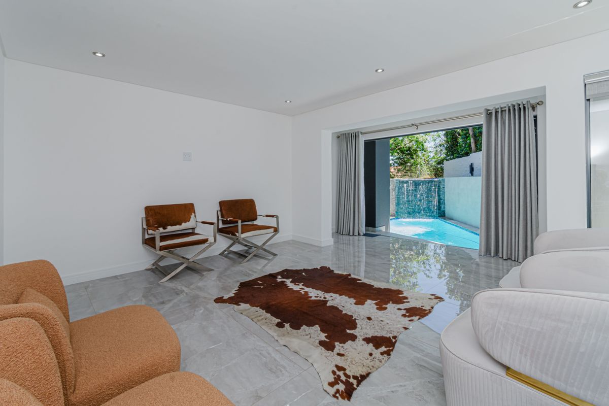 A bright, modern living room featuring large format floor tiles, recessed lighting, and seamless access to an outdoor pool area through sliding glass doors.