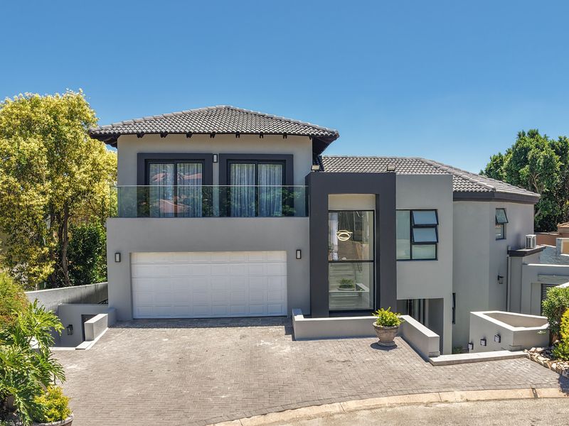 Modern double-storey residence featuring a paved driveway, double garage, and a sleek balcony with glass balustrades, set within a well-maintained residential environment.
