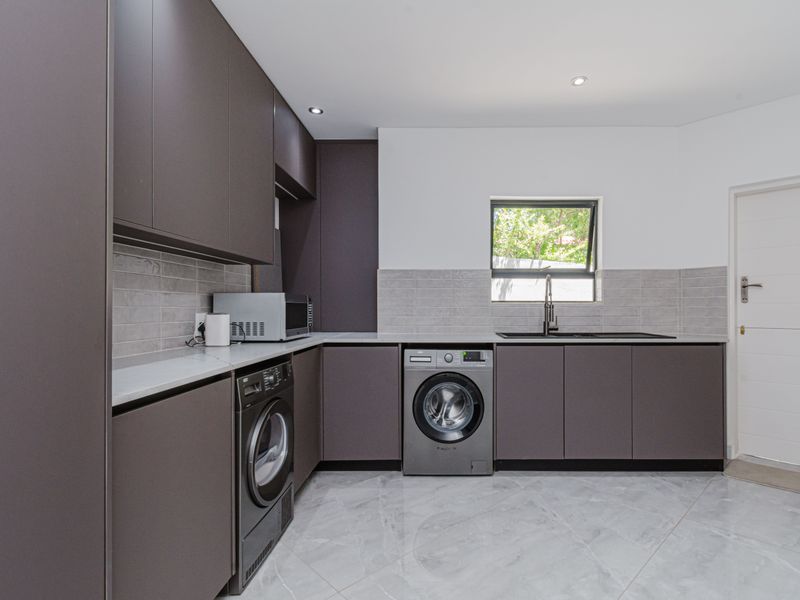 Modern laundry room featuring dark cabinetry, stone countertops, subway tile backsplash, undermount sink, and high-quality tiled flooring.
