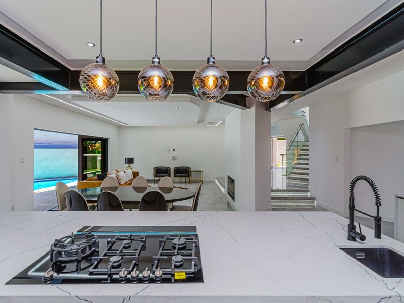Modern open-plan living area featuring a sleek kitchen island with gas hob, exposed steel beams, and a contemporary staircase with glass balustrade.
