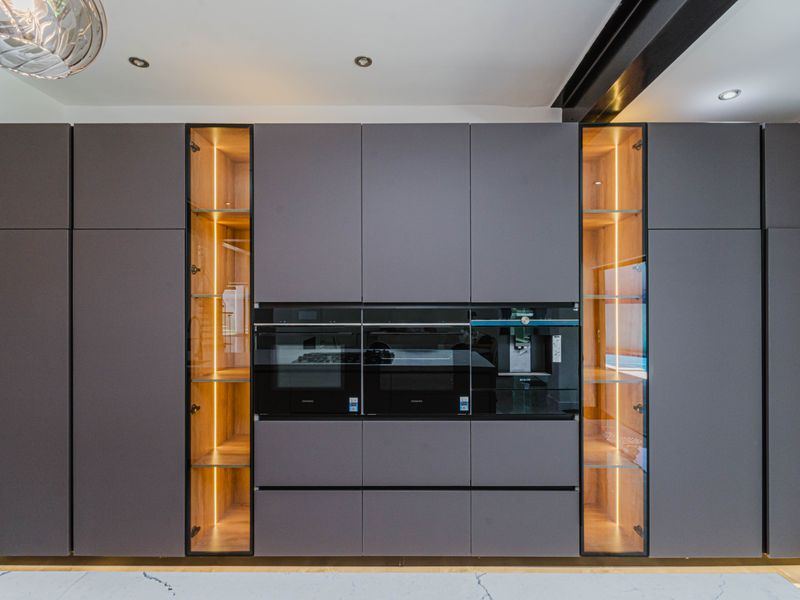 Modern kitchen featuring sleek handleless cabinetry, integrated high-end appliances, and illuminated glass display shelving for a sophisticated, contemporary aesthetic.
