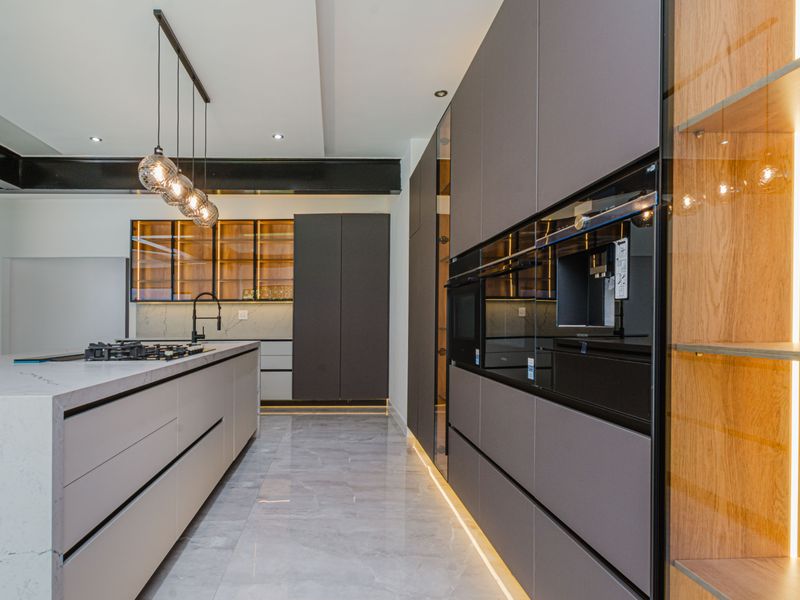 Modern, high-end kitchen featuring a large stone-topped island, integrated appliances, sleek matte cabinetry, and sophisticated under-cabinet and pendant lighting.