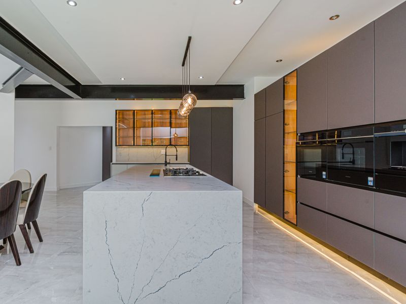 Modern luxury kitchen featuring a large marble island, high-end integrated appliances, sleek cabinetry, and sophisticated recessed lighting in an open-plan layout.