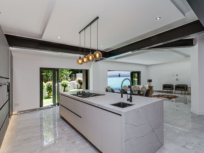 Modern open-plan kitchen and living area featuring a large marble-topped island, high-end built-in appliances, exposed steel beams, and seamless access to the outdoor space.