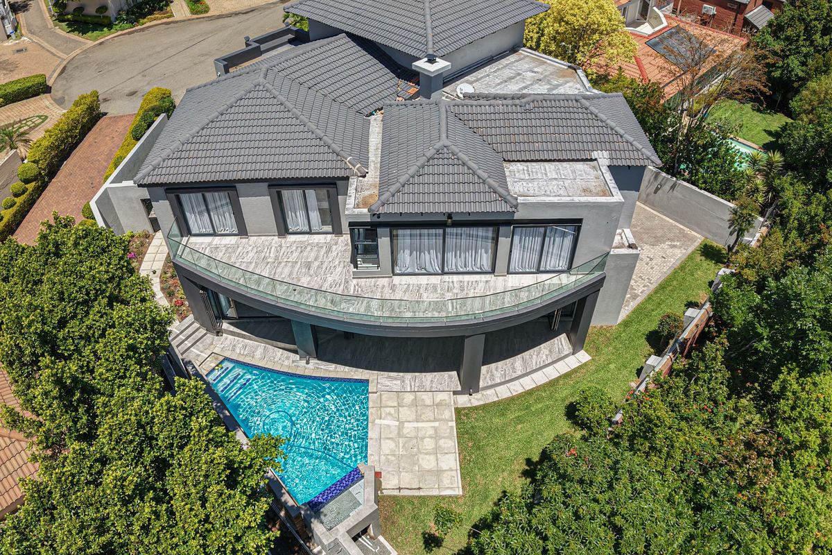 Aerial view of a modern double-story house featuring a tiled roof, a curved balcony with glass balustrades, and a private swimming pool.