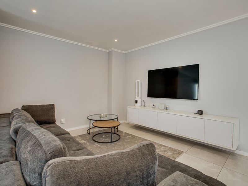 A modern living room featuring neutral tiled flooring, recessed downlighting, and a sleek wall-mounted media console.