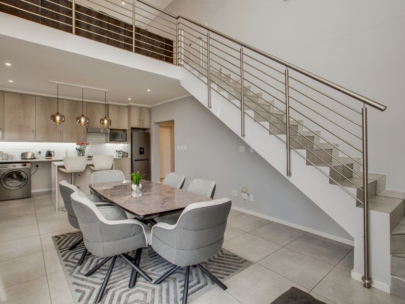 Modern open-plan living area featuring a sleek kitchen, dining space, and a striking staircase with stainless steel railings leading to a mezzanine level.