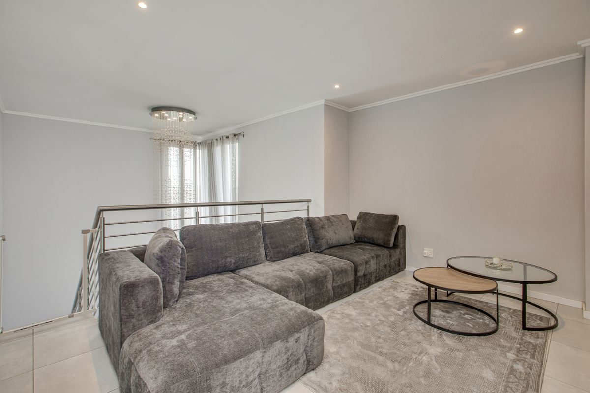 A well-maintained living area featuring tiled flooring, recessed downlighting, and a modern stainless steel balustrade overlooking the staircase.