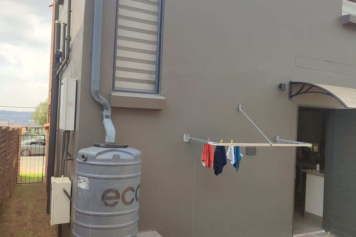 Rear exterior view of the townhouse featuring a water tank, wall-mounted drying rack, and a protective door canopy over the entrance.