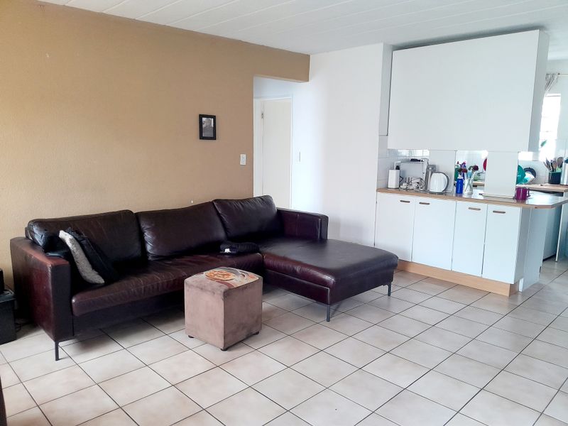Open plan living area featuring tiled flooring and a functional kitchen with white cabinetry and a breakfast counter.