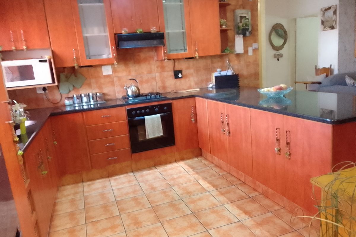 A functional kitchen featuring warm-toned wooden cabinetry, granite countertops, a built-in oven, gas hob, and tiled flooring throughout.