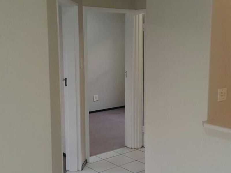 A clean, empty hallway featuring neutral wall paint, white tiled flooring, and access to adjacent rooms.