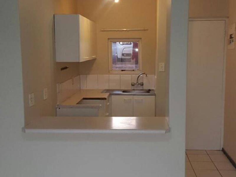 A compact, functional kitchen featuring white cabinetry, a tiled backsplash, a stainless steel sink, and a breakfast bar opening into the living area.