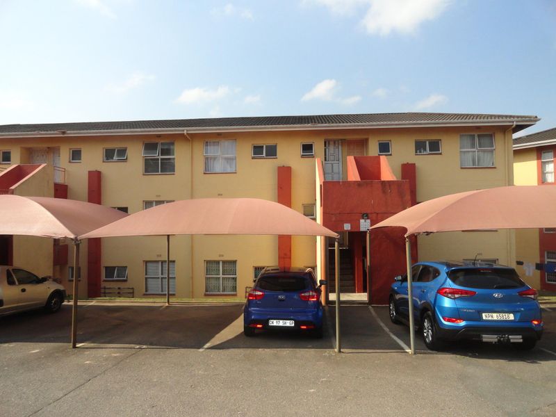 Exterior view of a multi-story apartment block featuring covered parking bays, external staircases, and security-fitted windows.