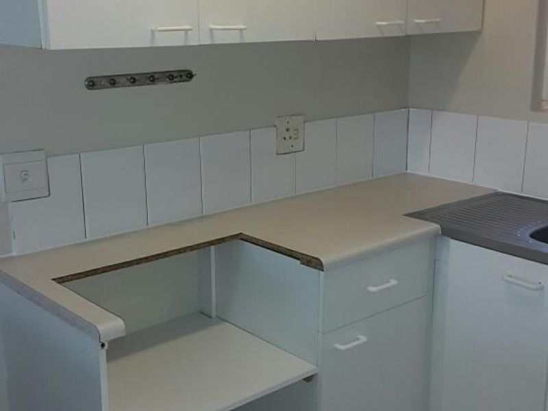 A functional kitchen area featuring white cabinetry, tiled backsplash, and tiled flooring, with a dedicated space for an under-counter appliance.