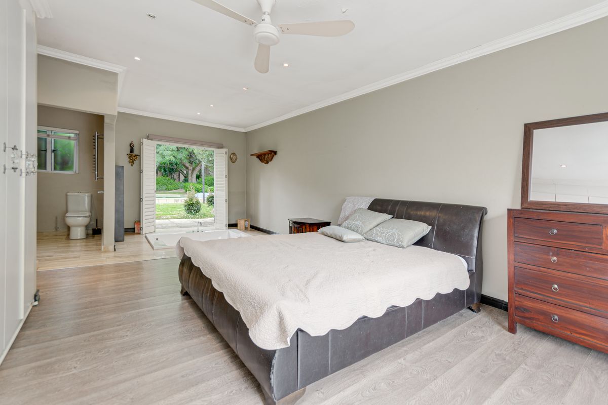Spacious bedroom featuring wood-look flooring, recessed lighting, a ceiling fan, and an open-plan en-suite bathroom with a soaking tub and direct garden access.