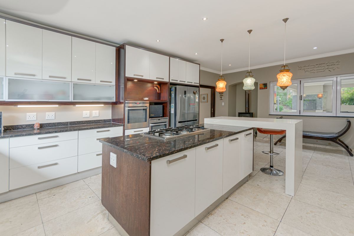 Modern kitchen featuring a central island with a built-in gas hob, stone countertops, high-gloss cabinetry, and integrated appliances, flowing into an open-plan living area.