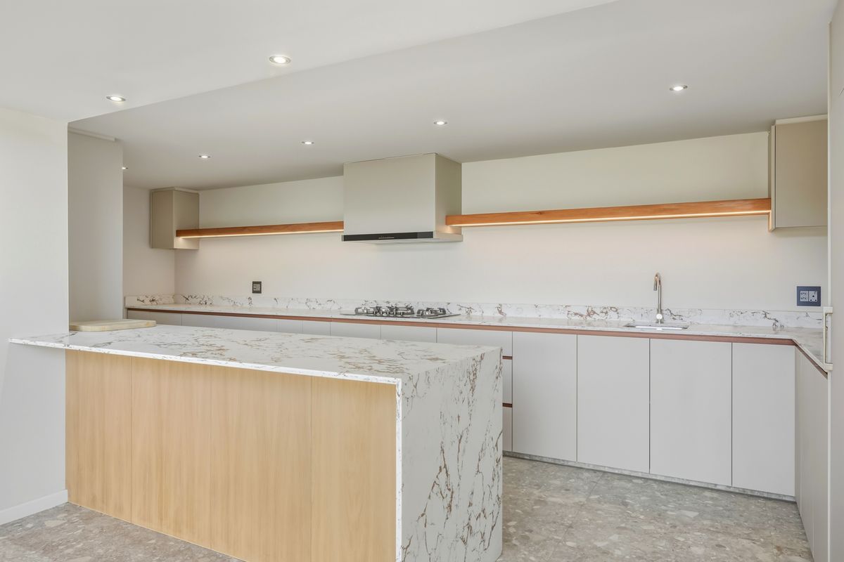 Modern kitchen featuring a marble-topped island, sleek cabinetry, integrated gas cooktop, extractor fan, and recessed ceiling lighting.