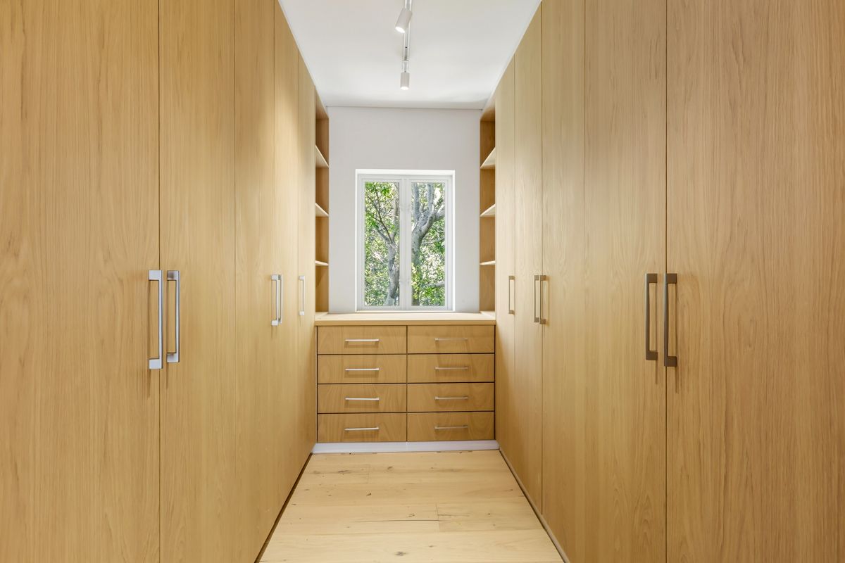 A well-appointed walk-in closet featuring extensive custom light oak cabinetry, integrated drawer units, and natural timber flooring with a bright window view.
