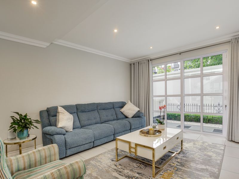A bright and well-maintained living room featuring tiled floors, crown molding, recessed lighting, and large glass doors providing access to the exterior.
