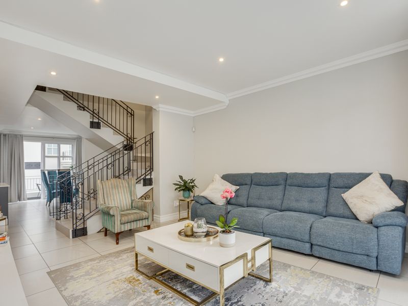 Open plan living area featuring tiled flooring, recessed lighting, and a decorative wrought iron staircase railing leading to the upper level.