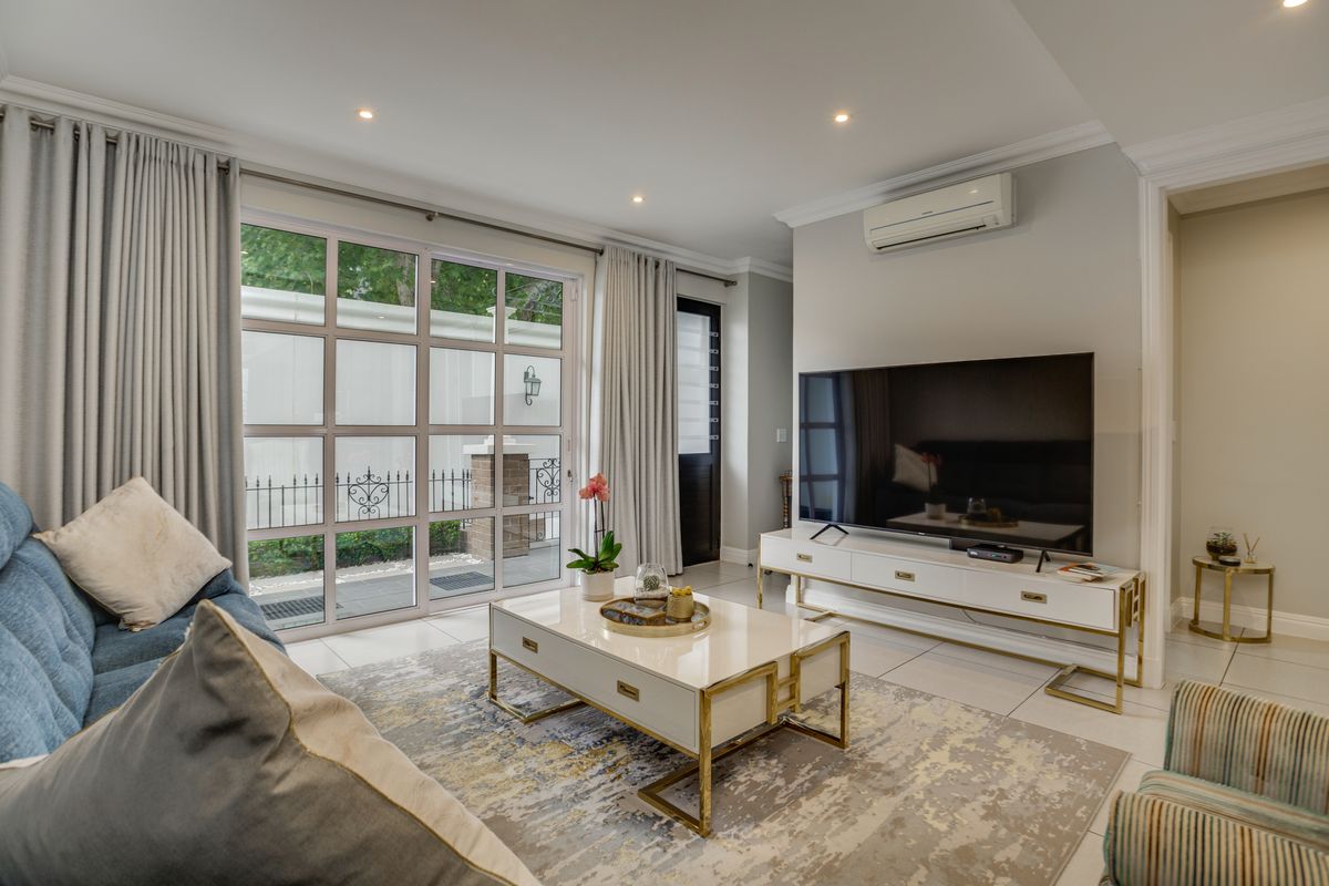 A bright and modern living room featuring tiled floors, recessed lighting, crown molding, and large glass sliding doors leading to an outdoor area.