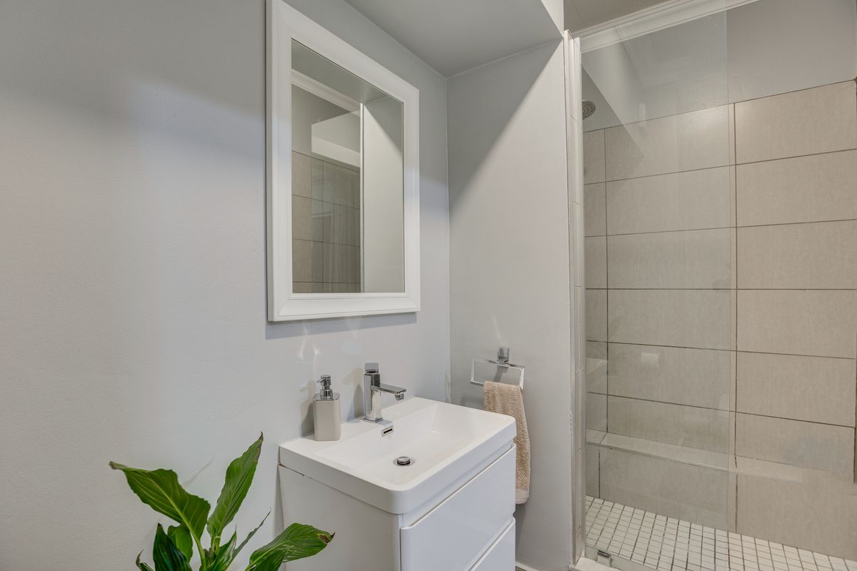 Modern bathroom featuring a sleek vanity with basin, wall-mounted mirror, and a glass-enclosed shower with neutral wall tiling.