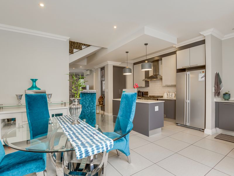 Modern open-plan kitchen and dining area featuring sleek cabinetry, a central island, subway tile backsplash, and elegant crown molding throughout the space.