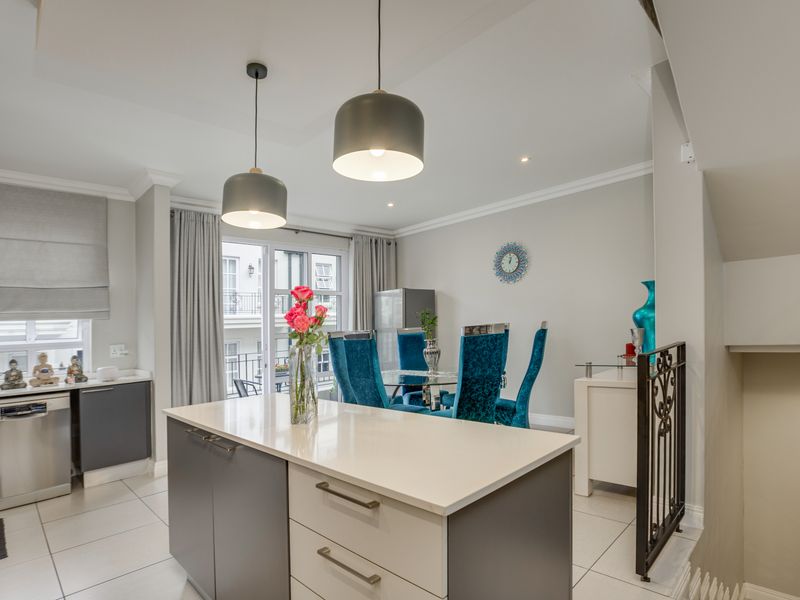 Modern open-plan kitchen and dining area featuring a central island with stone countertops, sleek cabinetry, tiled flooring, and elegant pendant lighting.