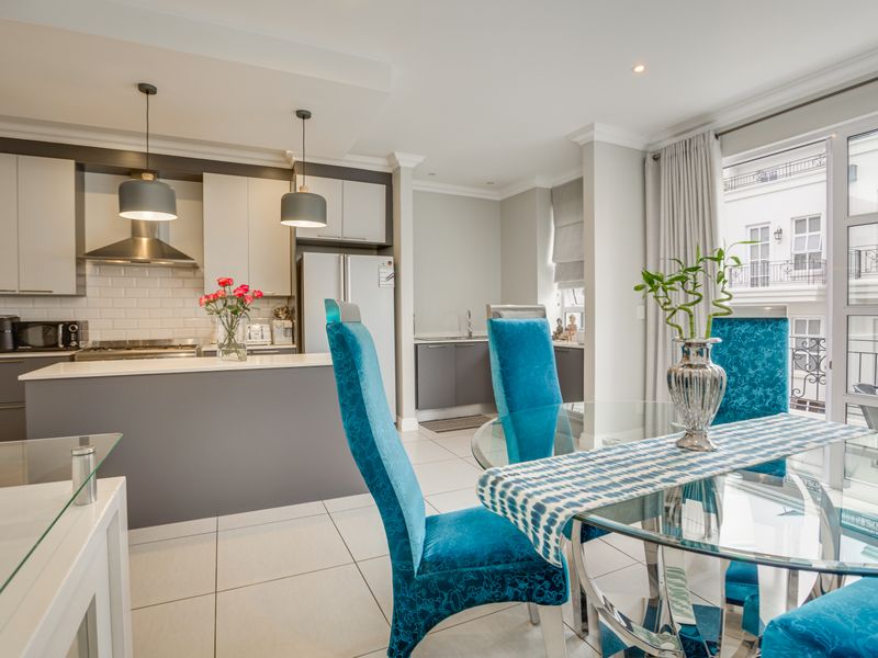 Modern open-plan kitchen and dining area featuring sleek cabinetry, stone countertops, subway tile backsplash, and direct access to a balcony through sliding glass doors.